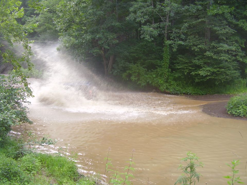 Vehicle hidden behind a huge wall of brown spray while blasting a muddy water hole