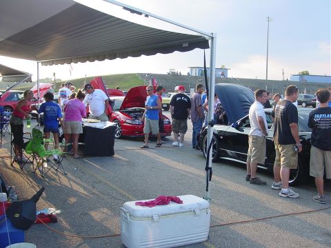 1986 Ford Mustang - An outdoor event with several cars and people mingling under a large canopy.