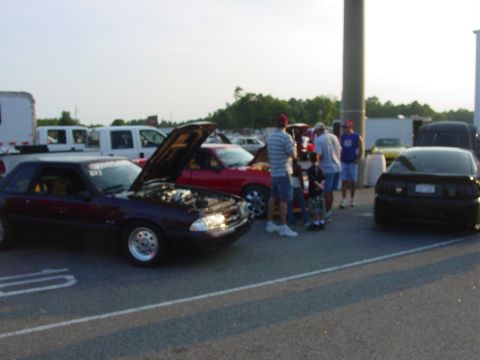 1986 Ford Mustang - A dark red Ford Mustang is displayed with its hood open, surrounded by onlookers.