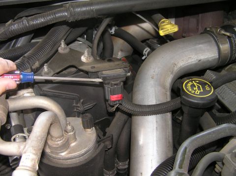 2000 Ford Excursion - Working on a sensor in the engine bay, with oil and transmission fluid caps visible.