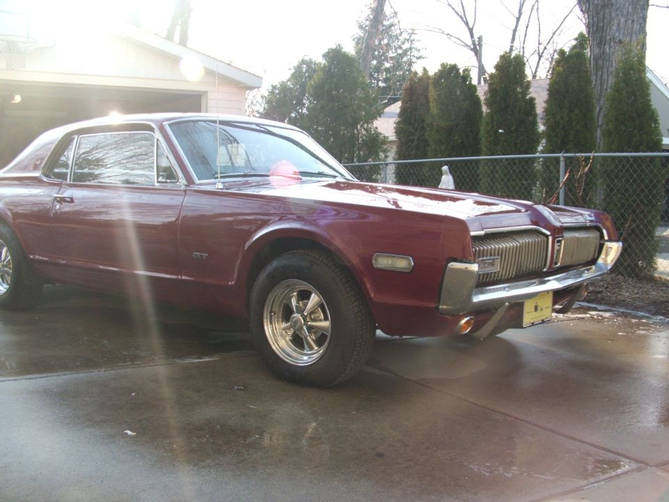 Dark red Mercury Cougar coupe parked on a wet driveway by a fence