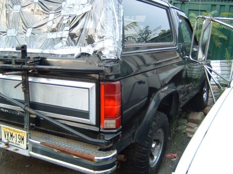 1986 Ford Bronco - The rear of a Ford Bronco shows a custom tarp covering the bed area, held on with tape and straps.