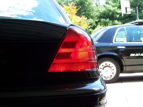 2003 Ford Crown Victoria - Close-up of a black car's tail light, with another black vehicle in the background.