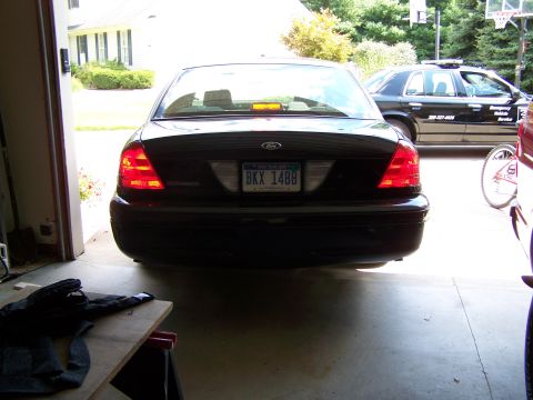 2003 Ford Crown Victoria - The rear of a black sedan is visible, parked in a garage. Another vehicle is parked outside.