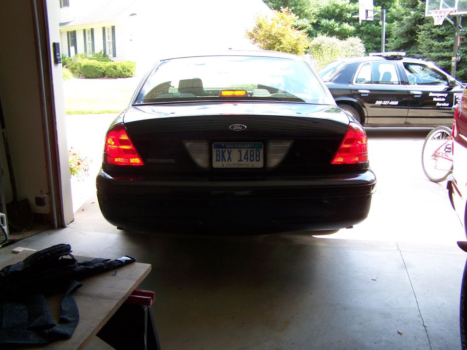 Rear view of a black 2003 Ford Crown Victoria parked in a garage, with another black vehicle visible outside
