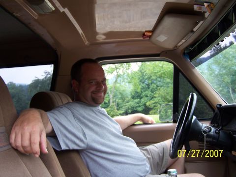 1979 Ford F-150 - A man smiles from the interior of a truck, with greenery visible through the window.