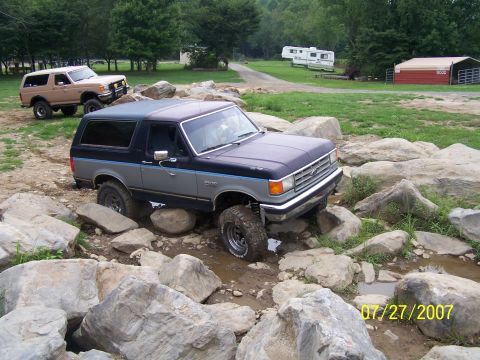 1979 Ford F-150 - Two Ford Broncos tackle a challenging off-road course with large rocks and water.