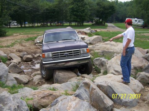 1979 Ford F-150 - A man directs a Ford Bronco through a challenging off-road course with large rocks and water.