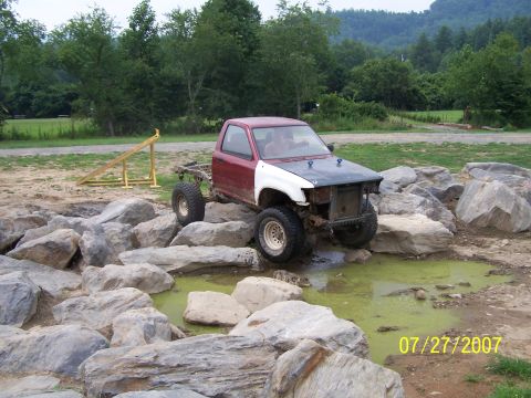 1979 Ford F-150 - A modified pickup truck navigates a rocky obstacle course with a muddy puddle.