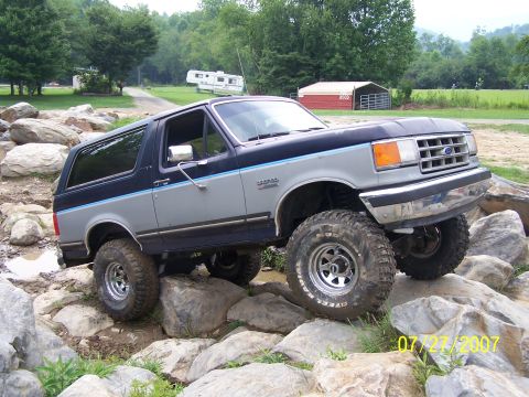 1979 Ford F-150 - A lifted Ford Bronco navigates a rocky terrain, its off-road tires gripping the stones.