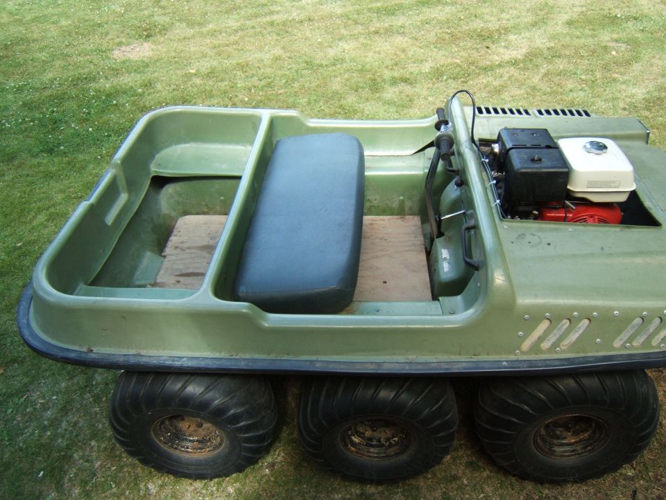 Green 6-wheeled amphibious ATV with black seat and Honda engine, parked on grass.