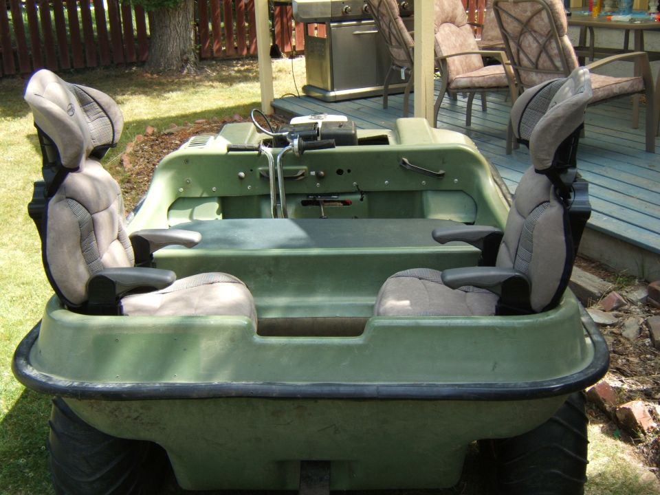 Green Argo amphibious ATV from rear with two gray bucket seats, parked on grass by a deck