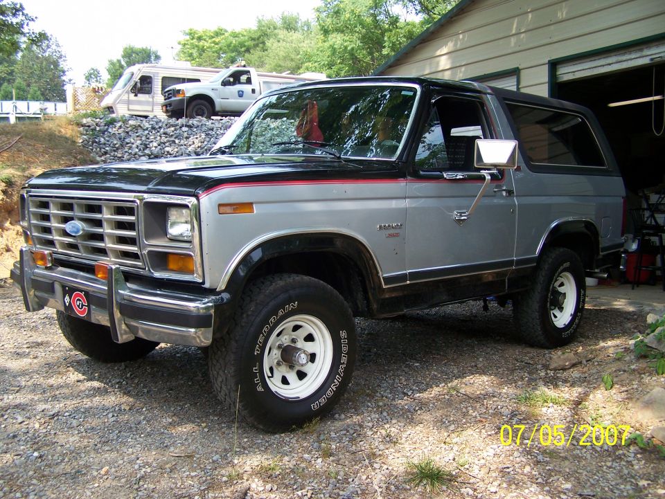 Black and silver 1980s Ford Bronco SUV, 3/4 front view on gravel