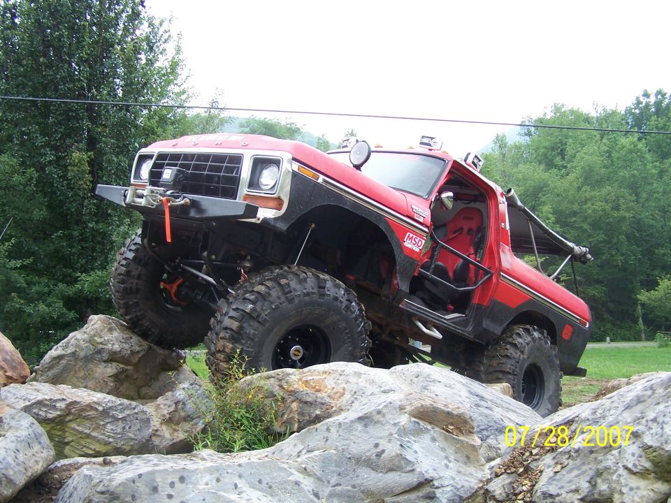Red 1979 Ford F-150 with large tires and off-road modifications climbing over rocks