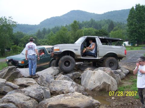 1979 Ford F-150 - Two off-road trucks are shown navigating a challenging rocky terrain on a cloudy day.