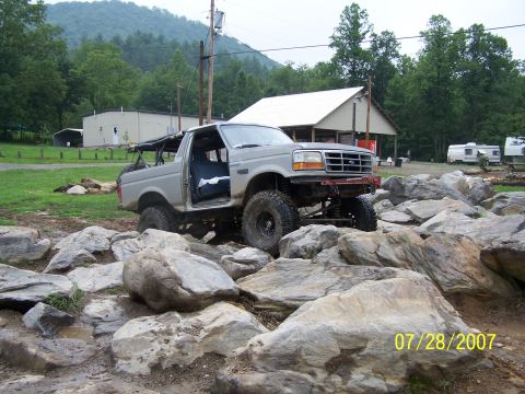 1979 Ford F-150 - A modified pickup truck tackles a challenging rocky terrain on a cloudy day.