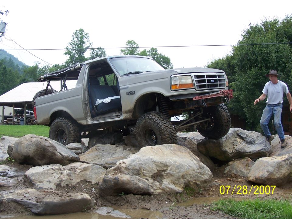 Gray Ford Bronco off-roading over rocks, driver's door open
