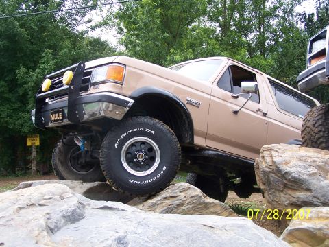 1979 Ford F-150 - This tan Ford Bronco is shown tackling a rocky terrain, equipped with all-terrain tires and auxiliary lights.
