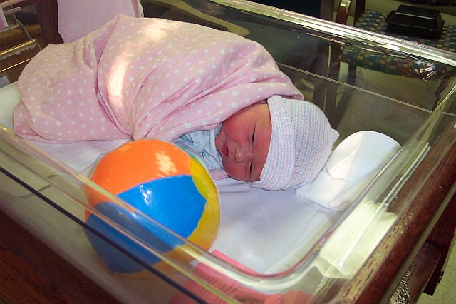 Newborn baby in a bassinet with a pink blanket and a colorful ball