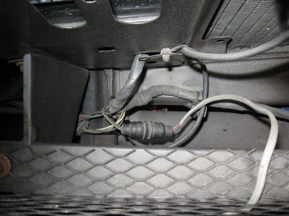 Close-up of vehicle wiring harness connected to a black rubber boot, with part of a radiator visible