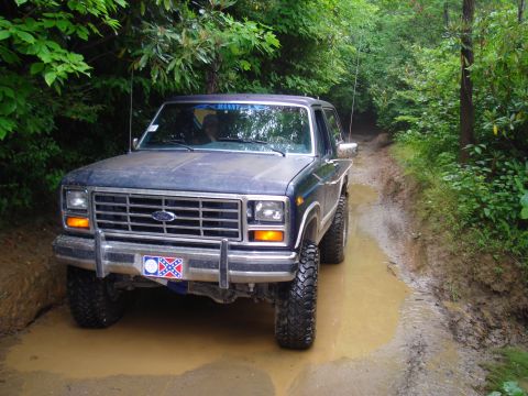 1984 Ford Bronco - This 1980 Ford Bronco navigates a muddy off-road path surrounded by dense foliage.