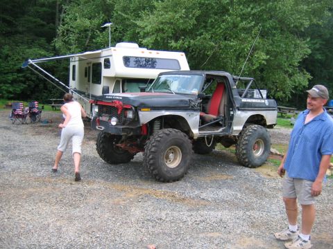1992 Ford Mustang - A heavily modified pickup truck with large off-road tires is parked next to a recreational vehicle in a gravel lot.