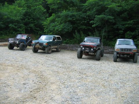 1992 Ford Mustang - A collection of four off-road vehicles are parked in a gravel lot surrounded by dense foliage.