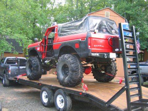 1992 Ford Mustang - A lifted red Ford Bronco with a soft top is loaded onto a trailer, with a gray pickup truck visible beside it.