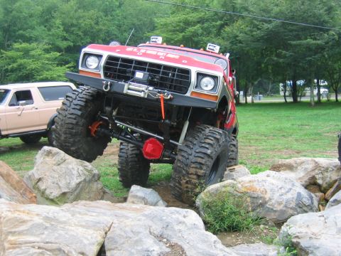 1992 Ford Mustang - A heavily modified red truck with oversized tires is shown off-roading over large rocks.