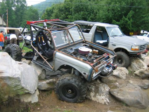 1992 Ford Mustang - This heavily modified off-road vehicle, possibly a custom buggy, is positioned next to a pickup truck on a rocky terrain.