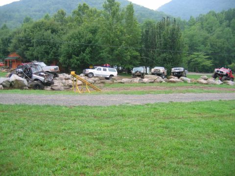 1992 Ford Mustang - Several modified trucks and SUVs are positioned on a large rock formation, indicating an off-road event.