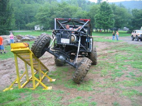 1992 Ford Mustang - A custom-built off-road buggy navigates a challenging obstacle course, with one wheel elevated on a yellow ramp.