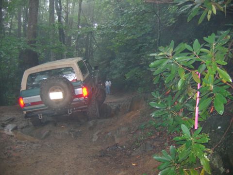 1992 Ford Mustang - A Ford Bronco navigates a challenging, muddy off-road path through a wooded area.