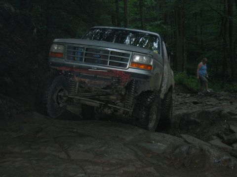 1992 Ford Mustang - A lifted Ford Bronco navigates a challenging off-road course in a wooded area.