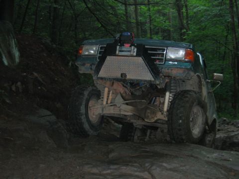 1992 Ford Mustang - This green off-road vehicle, equipped with a front winch, navigates a challenging rocky path through a wooded area.