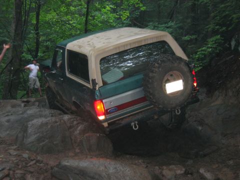 1992 Ford Mustang - A Ford Bronco is shown navigating a rocky, off-road trail with trees in the background.