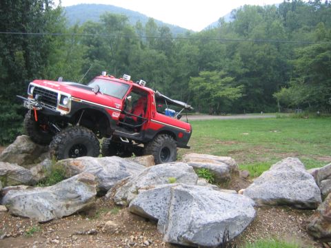 1979 Ford Bronco - This modified SUV is shown off-roading over large rocks in a wooded area.