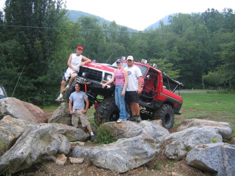 1979 Ford Bronco - A group poses with a heavily modified red 1979 Ford Bronco, positioned amongst large rocks in a scenic outdoor setting.