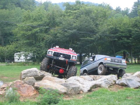 1979 Ford Bronco - Two modified SUVs navigate a rocky obstacle course in a wooded area.