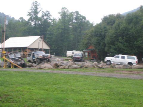1979 Ford Bronco - Several off-road vehicles are positioned on a rocky area with trees and buildings in the background.
