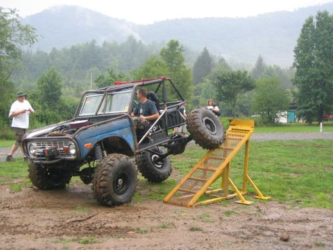 1979 Ford Bronco - Modified off-road vehicle with a roll cage is positioned on a muddy terrain near a yellow ramp.