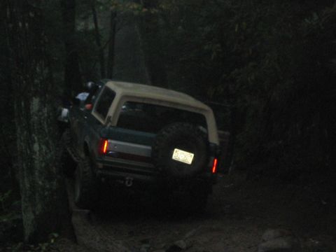 1979 Ford Bronco - Ford Bronco navigates a wooded trail at dusk, showing its rear and spare tire.