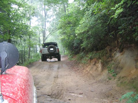 1979 Ford Bronco - Two SUVs on a muddy, wooded trail. The lead vehicle is partially visible in the foreground.