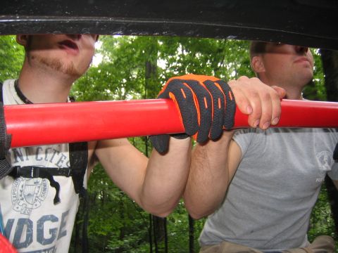 1979 Ford Bronco - Two men hold onto a red bar inside a vehicle, with one wearing orange and black work gloves.
