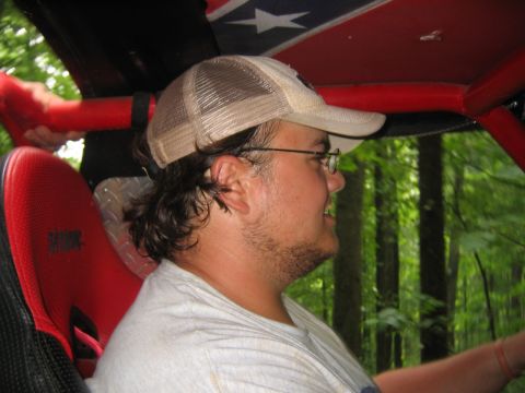 1979 Ford Bronco - A man with a beard and glasses drives an off-road vehicle through a wooded area.