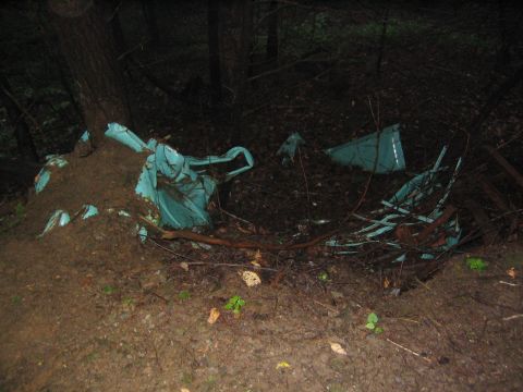 1979 Ford Bronco - Wreckage of a teal-colored vehicle is visible, partially covered by dirt and debris, in a wooded area.