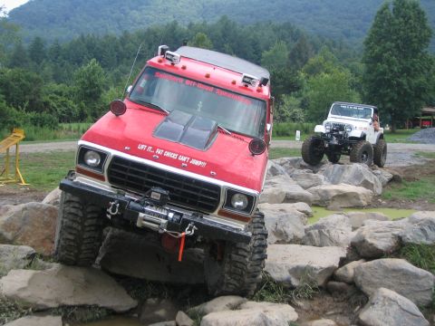 1979 Ford Bronco - A red off-road vehicle tackles a rocky obstacle course, with another Jeep in the background.