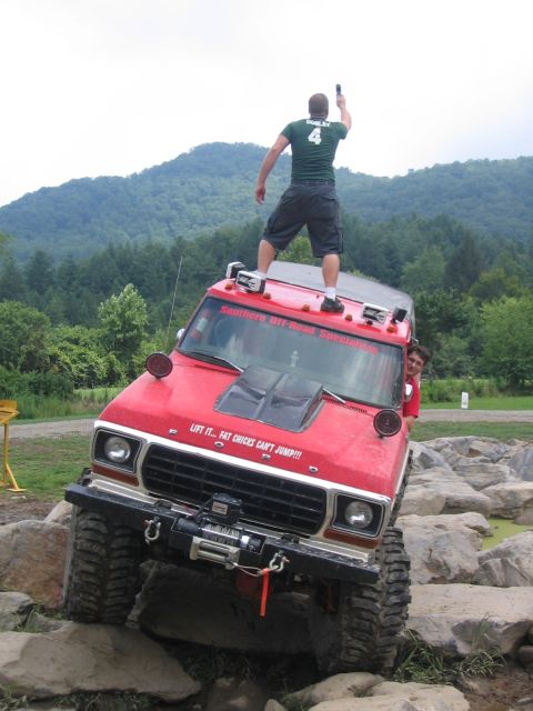 1979 Ford Bronco - A red 1979 Ford Bronco navigates a rocky obstacle course, with a person standing on its roof.