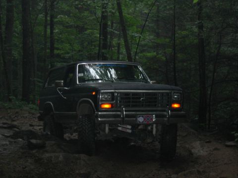 1992 Ford Mustang - A dark colored Ford Bronco navigates a rocky, wooded trail.