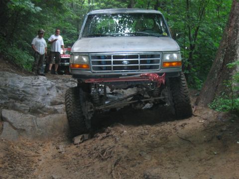 1992 Ford Mustang - A lifted Ford Bronco navigates a challenging off-road course with two people watching.